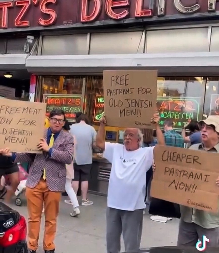 People protesting with humorous signs in front of Katz's deli