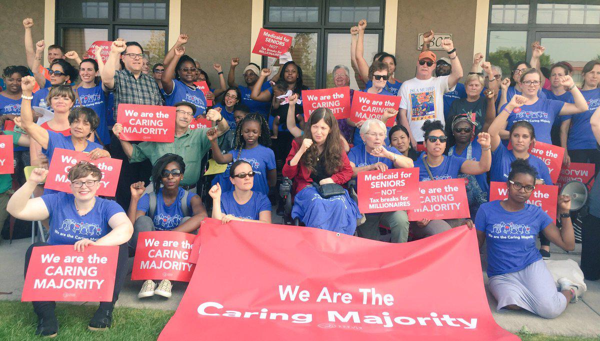 Members of the caring majority caucus gather with matching shirts and signs saying We Are The Caring Majority